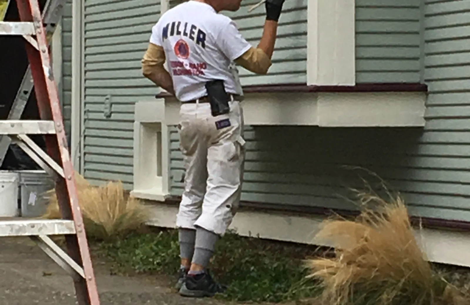 A G & F painter on a ladder cutting in exterior trim on a Portland house