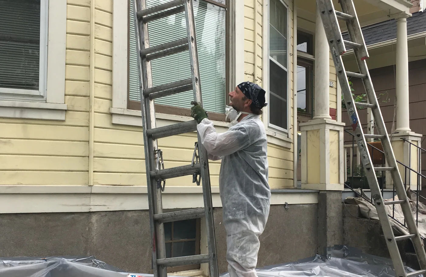Ladders and drop cloths set up against a gable during exterior prep