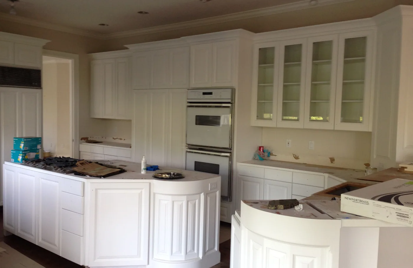 White kitchen with glass-front uppers and a curved island, mid-project