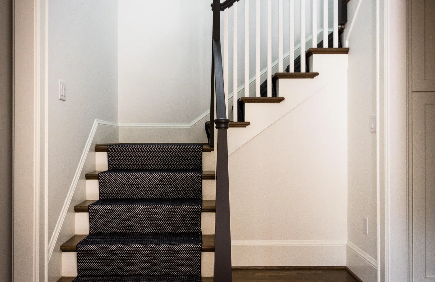 White stair with a dark handrail and a striped runner