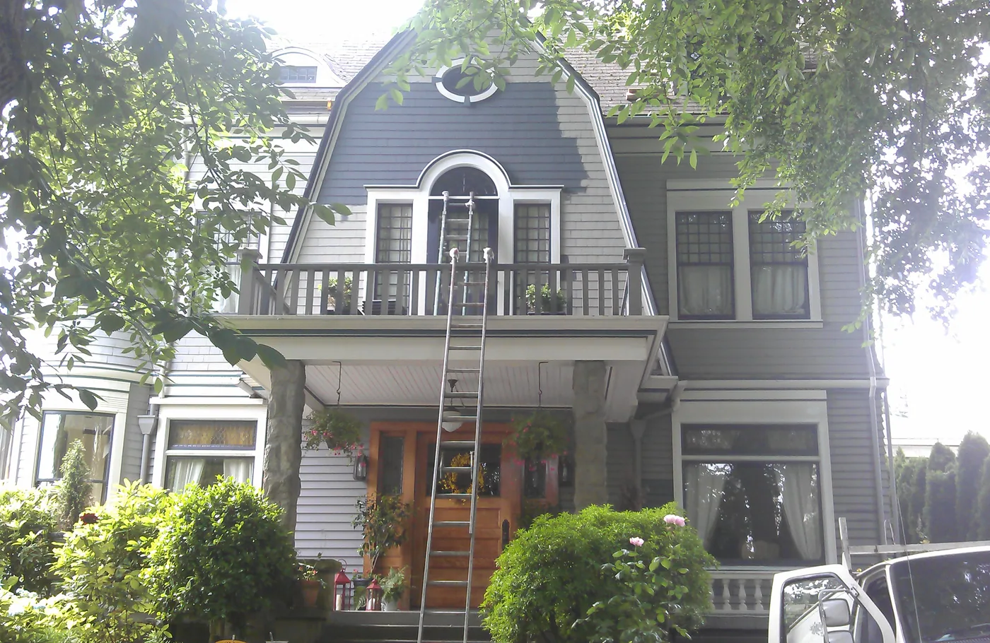 Ladders up on a grey-blue gambrel home during an exterior repaint