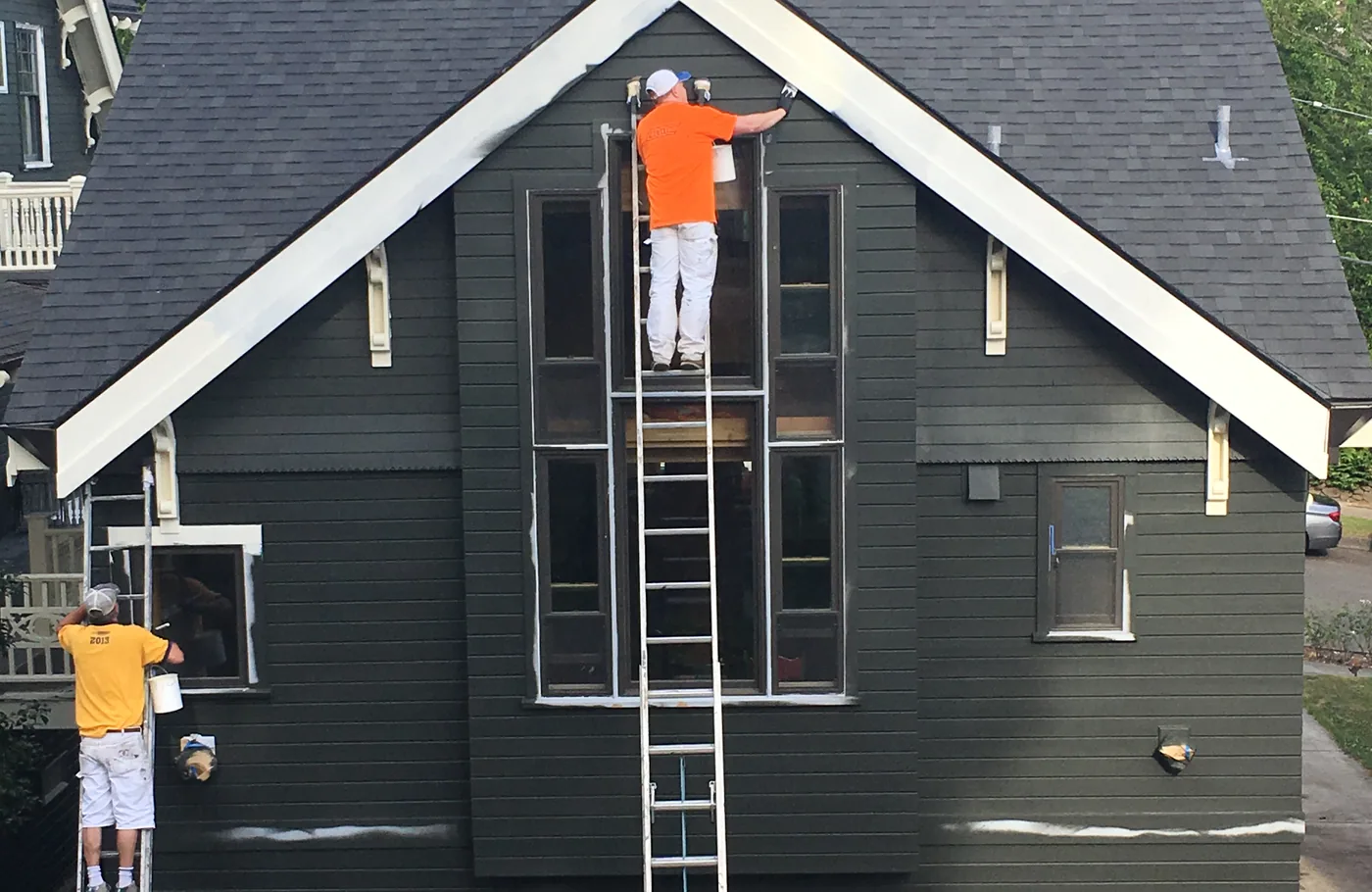 Crew on ladders painting white trim on a charcoal home