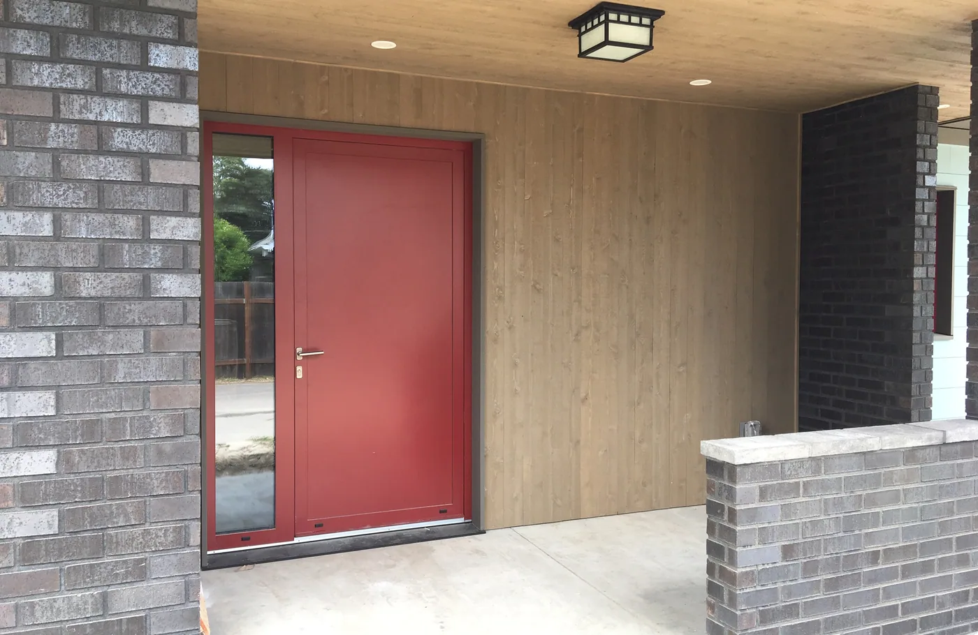 Modern entry with a red door and a wood-lined porch ceiling